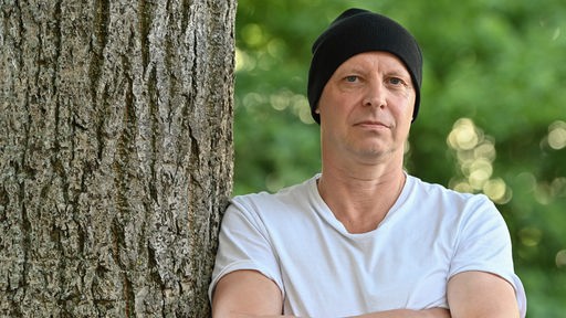 Dramatiker und Regisseur Armin Petras, er lehnt mit verschränkten Armen an einem Baum.