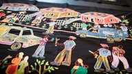 Kunstwerke des Artivism Atrocity Prevention Pavillons des Auschwitz Instituts Peace and Reconciliation: Stickerei zeigt Polizeiautos, die durch eine Nachbarschaft mit spielenden Kindern und sich unterhaltenden Erwachsenen fahren.