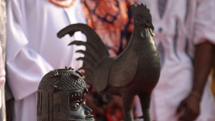 Benin Bronzen in Form eines Hahns und einer Büste stehen auf einem Tisch.