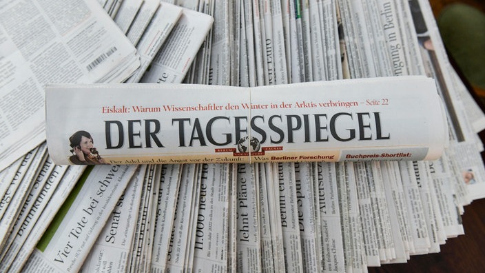 Zeitung "Der Tagespiegel" liegt zusammengerollt auf einem Haufen weiterer Zeitungen.