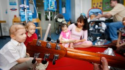 Musizieren mit Kindern im Krankenhaus, Kinder sitzen im Kreis auf dem Boden in einem Krankenhauszimmer, jemand spielt Gitarre.