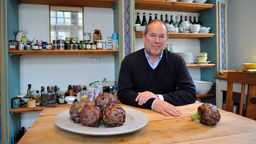 Wein- und Kulinarikexperte Otto Geisel sitzt in einer Küche an einem Tisch.