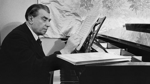 Der Komponist Reinhold Glière sitzt am Klavier und schreibt auf ein Notenblatt.