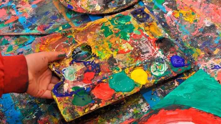 Eine kindliche Hand hält eine mit bunten Farben verschmierte Farbpalette.