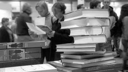 Ein Bücherstapel und Besucher*Innen auf der Leipziger Buchmesse