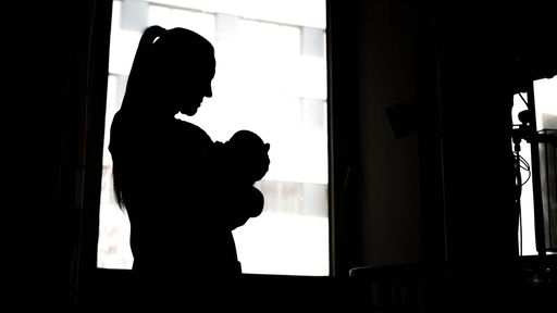 Eine Frau steht mit einem Neugeborenen am Fenster der Klinik.