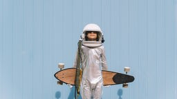 Ein Junge in Astronauten-Kostüm hält ein Longboard in den Armen.