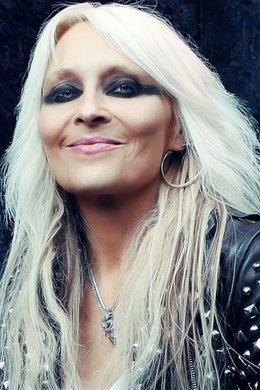 Die Rock-Sängerin Doro Pesch lächelt in die Kamera, sie hat lange blonde Haare und trägt dunkles Augenmakeup, dazu eine schwarze Jacke mit Nieten.