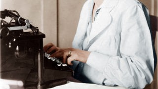Zu sehen ist der Oberkörper einer Frau, welche auf einer Schreibmaschine tippt.