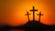 Drei schwarze Kreuze auf einem Hügel, der Hintergrund orange.