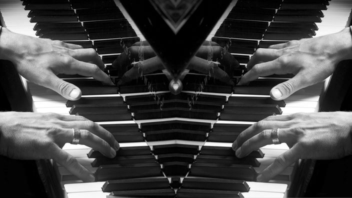 Schwarz-weiß Bild gespiegelt: Hände spielen Klavier.