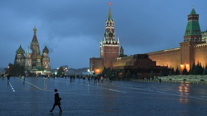 Wenige Passanten gehen am Abend in Moskau bei herbstlichem Nieselregen vor der Kulisse der Basilius-Kathedrale (l) und der Kreml-Mauer über den Roten Platz.