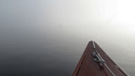 Spitze eines kleinen Bootes, das bei Nebel auf einem See treibt.