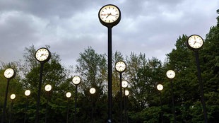 Mehrere Uhren der Installation 'Zeitfeld' von Klaus Rinke vor verdunkeltem Himmel.