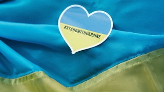 Auf einer Ukraine-Flagge liegt ein Herz-Aufkleber mit der Aufschrift "I stand with Ukraine".