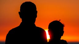 Vater und Sohn stehen mit dem Rücken zur Kamera vor einem Sonnenuntergang.