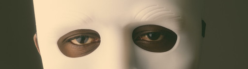 Ein Schwarzer Mann trägt eine weiße Maske und hält einen Finger vor seinen Mund.