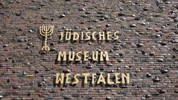 Die Fassade des Jüdische Museum Westfalen in Dorsten mit dem gleichnamigen, goldenen Schriftzug mit dem Logo eines siebenarmigen Leuchters.