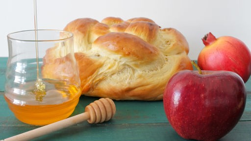 Ein runder Laib süßes Brot (Challah), Äpfel und eine Schale voller Honig.