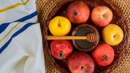 Das Bild zeigt eine traditionelle Süßspeise des jüdischen Neujahrsfest: Äpfel und Granatäpfel sind rund um einen Honigtopf arrangiert.