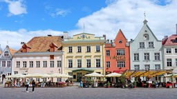 Rathausplatz in Tallinn: Schmale, bunte Häuser mit spitzen Giebeln vor denen Restaurants Tische, Stühle und Schirme aufgestellt haben.