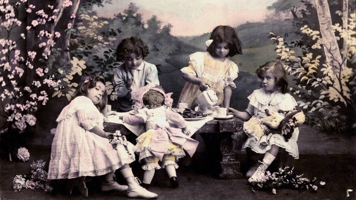 Historische Fotografie: Mädchen spielen im Freien mit Puppen an einer Kaffeetafel.