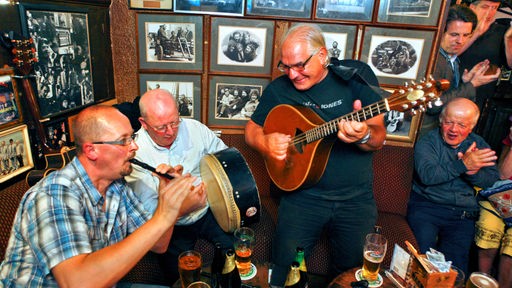 Musiker mit ihren traditionellen Instrumenten um einen Tisch mit Getränken in einem Irish Pub