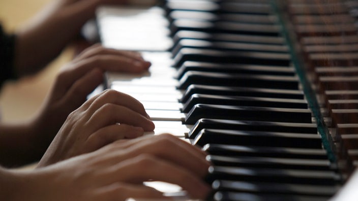 Nahaufnahme von vier Händen, die auf einem Klavier spielen.
