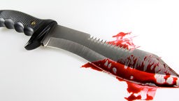 Ein Messer mit Kunstblut liegt auf einem weißen Untergrund.