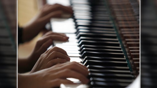 Nahaufnahme von vier Händen, die auf einer Klaviatur spielen.
