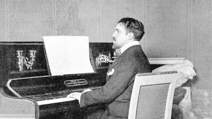 Schwarz-Weiß-Porträt von Reynaldo Hahn an einem Klavier.