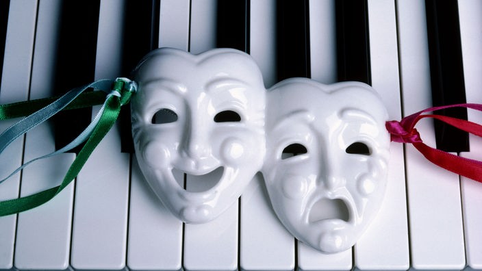 Eine lachende und eine weinende Maske liegen auf der Tastatur eines Klaviers.