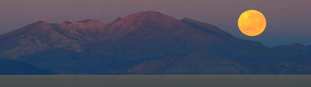 Vollmond im Morgengrauen, der hinter sich hinter einem Berg am Meer absenkt.