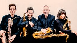 Portrait des Raschèr Saxophone Quartets - sitzend mit Saxohponen in den Händen