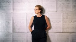 Die Komponistin Rebecca Saunders steht vor einer Wand mit Notenblättern