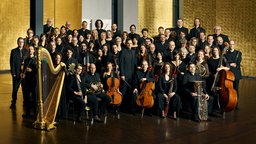 Die Mitglieder des Sinfonieorchesters Aachen sind in einem Gruppenfoto mit ihren Instrumenten zu sehen. 
