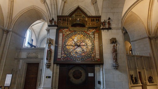 Innenansicht vom vom St. Paulus Dom in Münster: Eine knapp 8 Meter hohe, reich verzierte Uhr hängt im südlichen Chorumgang. 