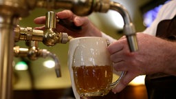 Ein Barkeeper zapft ein Glas Bier in einer Kneipe.