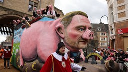 Ein Motivwagen, der Bundesfinanzminister Christian Lindner als Sparschwein zeigen soll, fährt im Rosenmontagsumzug mit.