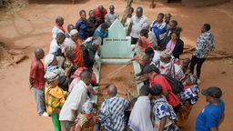 Filmszene aus "Das leere Grab": Mehrere Menschen stehen um ein Grab mit der Inschrift "Nduna Songea Mbano".