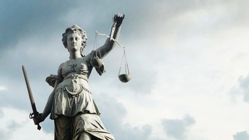 Die Statue der Justitia als Symbol für Gerechtigkeit vor blauem, bewölkten Himmel