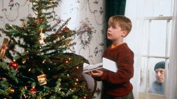 Filmszene von "Kevin allein zu Haus": Kevin vor einem Weihnachtsbaum, durch ein Fenster blickt ein Gangster ins Haus