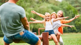 Lachende Kinder und Eltern balancieren zusammen auf einer Schaukel.