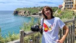 Die italienische Konzeptkünstlerin Lisa Borgiani psoiert mit ihrer Kamera vor einer Bucht.