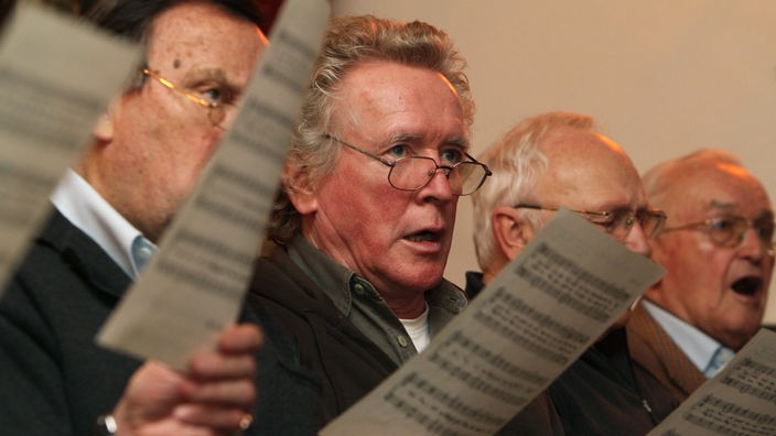 Mehrere Männer halten Notenblättern in der Hand und singen