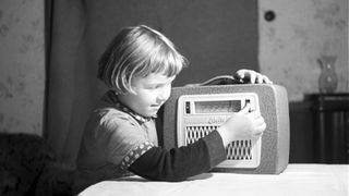 Das Beitragsbild des Dok5 "Der andere Kanal" zeigt eine schwarzweiß Fotografie eines Mädchen in der DDR mit dem Kofferradio Libelle, 1957 .