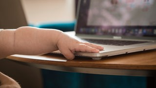 Die Hand eines Saeuglings liegt auf einem Laptop