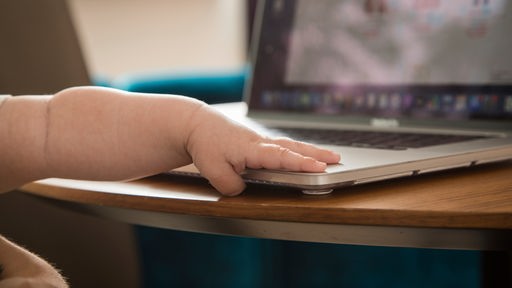 Die Hand eines Saeuglings liegt auf einem Laptop