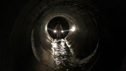 Das Beitragsbild des WDR3 "Reprogrammiert euch!" zeigt einen Kanalarbeiter mit einer Taschenlampe in einem dunklen Schacht in der Kanalisation. 