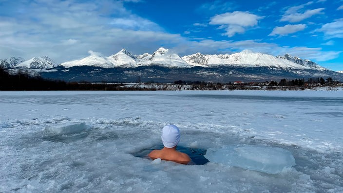 Eine Person schwimmt in Eiswasser und blickt auf die Berge.